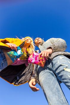 two people standing next to each other holding shopping bags and looking up into the sky