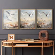 three paintings hang on the wall above a table