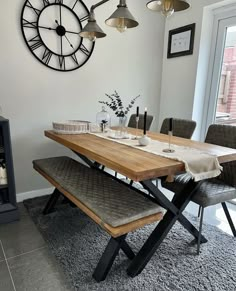 a dining room table with two benches and a clock on the wall in the background