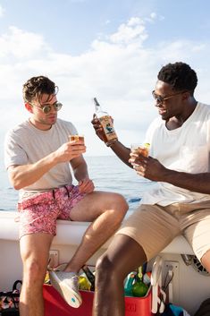 two men sitting on the back of a boat drinking beer and having fun with each other