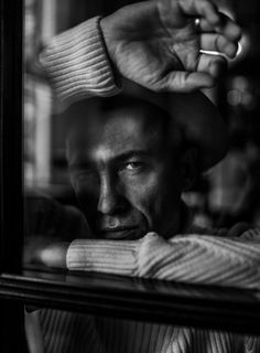 a black and white photo of a man looking in the mirror with his hand on his head