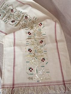 an embroidered white scarf with red and green trimmings on the edge, sitting on a bed