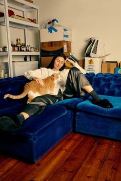 a woman sitting on top of a blue couch with a cat laying on her lap