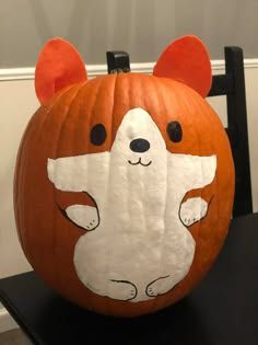 a carved pumpkin with a bear on it's face and ears, sitting on a chair