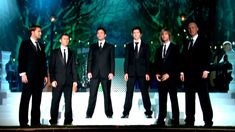 a group of men standing on top of a stage wearing black suits and white ties