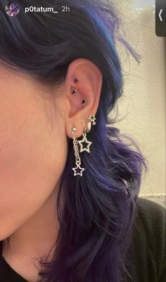 a close up of a person with blue hair wearing earrings and black shirt