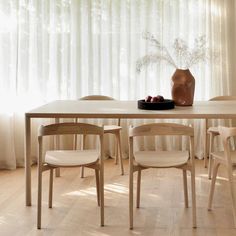 a dining table with chairs and a vase on top of it in front of a curtained window