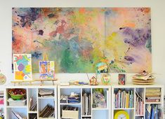 an art work hangs on the wall above a bookshelf filled with children's artwork