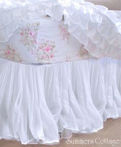 a white bed with ruffled bedspread and pink flowers on the bottom layer