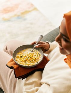 a woman sitting on a couch holding a bowl of food with a spoon in it