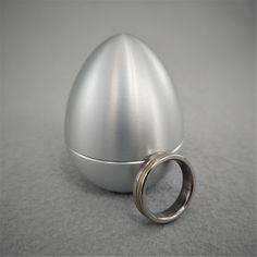 an egg shaped object sitting on top of a table next to a wedding ring in front of it