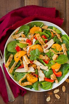 a salad with chicken, oranges and spinach in a white bowl on a wooden table