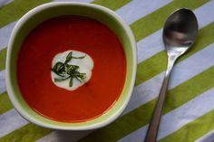 a bowl of tomato soup and a spoon on a striped tablecloth with green stripes