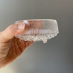 a hand holding a glass bowl with water on it's rim, in front of a gray background