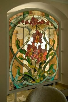 a stained glass window with flowers and leaves in the center, on a wall next to a chair