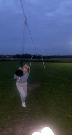 a woman swinging a baseball bat on top of a lush green field in the evening