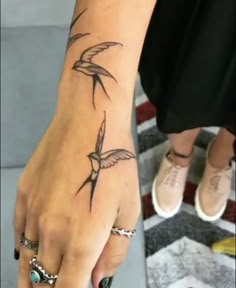 a woman's hand with a bird tattoo on her left wrist and two rings