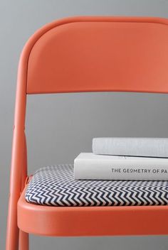 a stack of books sitting on top of an orange chair next to a white book