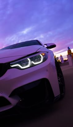 the front end of a purple car with its lights on at dusk in an urban setting