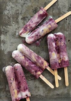 three popsicles with blueberry toppings sitting on top of a cement surface next to each other