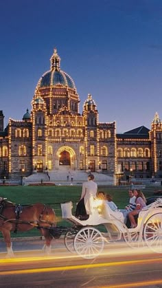 a horse drawn carriage in front of a large building with lights on it's sides