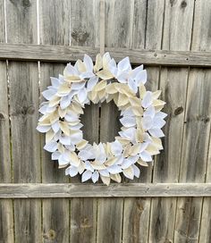 a wreath made out of white paper flowers on a wooden fence next to a green plant