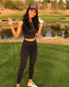 a woman holding a golf club in her right hand and posing for a photo on the golf course