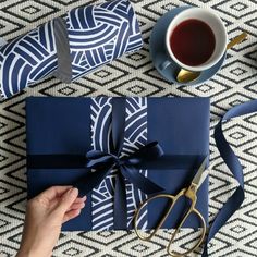 a person opening a blue gift box on top of a table next to a cup of coffee