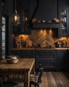 a kitchen with wooden floors and black cabinets, an island table and two pendant lights hanging from the ceiling