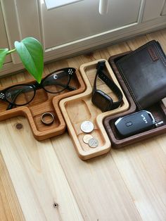 a wooden tray with glasses, cell phone and wallet on it next to a potted plant