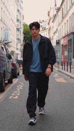 a young man walking down the street in front of parked cars