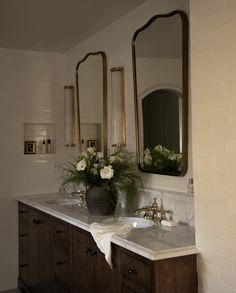 a bathroom with two sinks, mirrors and flowers in vases on the counter top