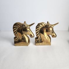 two golden unicorn figurines sitting next to each other on a white table top