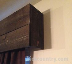 the corner of a room with curtains and a wooden box hanging on it's wall