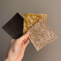 a hand is holding three different types of tiles on the wall, one brown and one beige