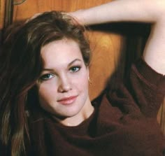 a woman with long brown hair and blue eyes posing in front of a wooden door