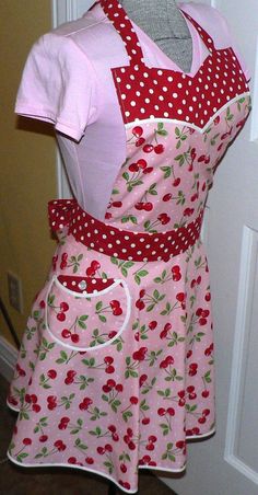 a pink apron with red polka dots and cherries on it is next to a mannequin