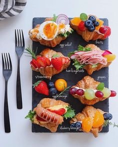 an assortment of fruits and pastries are displayed on a slate board with silverware