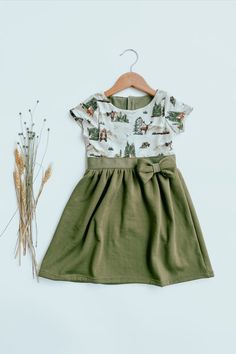 a green dress next to some dried flowers and a wooden hanger on a white background