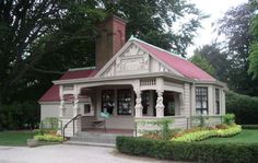 a small white house with a red roof in the middle of some trees and bushes