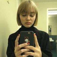 a woman is looking at her cell phone in the bathroom while wearing a black turtle neck sweater