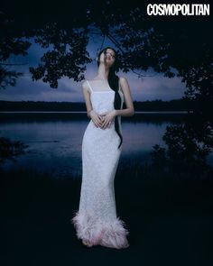 a woman in a white dress is standing by the water