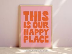 this is our happy place print in pink and orange on a wooden frame against a wall