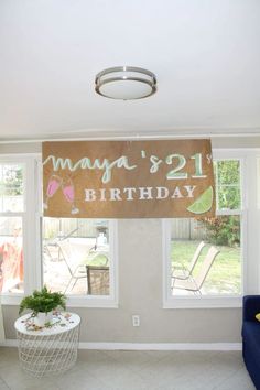 a happy 21st birthday banner hanging from the ceiling in a living room with two windows