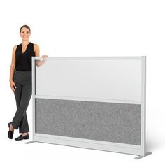 a woman standing next to a white and gray privacy panel divider with grey carpeting