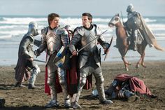 two men dressed in knight costumes standing on the beach next to another man wearing armor