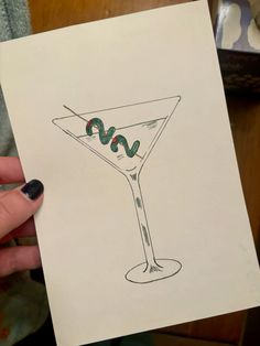 a drawing of a martini with a green snake on the rim