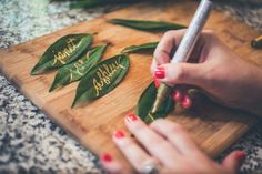 a woman is writing on some leaves with a pen in her hand while she sits at a table