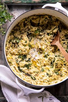 a pot filled with pasta and spinach on top of a wooden table