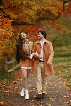 a man and woman walking down a path in an autumn park with leaves on the ground